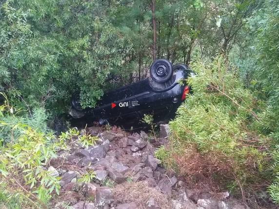 Bombeiros precisaram cortar porta e suspender o veículo para resgatar o condutor, que teve o braço preso após queda em ribanceira; chuva e neblina dificultaram o socorro