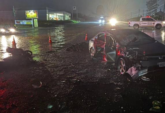 Colisão entre carro e motocicletas ocorreu no trevo de acesso ao município; terceira vítima foi socorrida em estado grave após possível aquaplanagem do veículo